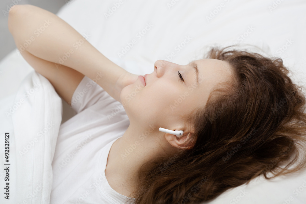 Beautiful brunette girl is lying on bed with wireless headphones listening to music Beautiful brunette girl is lying on bed with wireless headphones listening to music
