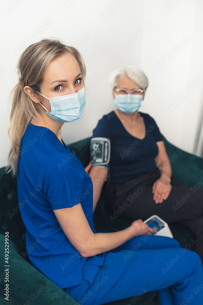 Taking care of health during coronavirus pandemic. Masked professional worker, and her patient sitting together on a sofa. High quality photo