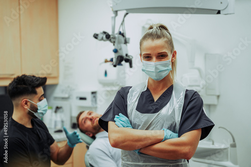 Caucasian female dentist wearing surgical mask standing with arms crossed in doctors room 