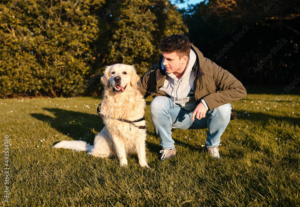 Caucasian boy standing with a golden retriever dog in a green park Caucasian boy standing with a golden retriever dog in a green park
