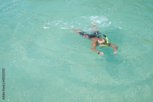 Top view of blond boy in the mask with the snorkel, he swimming and snorkelling in the blue transparent water. Sport concept. Childhood theme. copy space