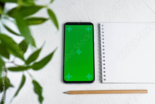Green leave with blank notepad smartphone green screen mockup and pencil flat lay. Top view