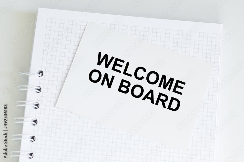 Obraz premium welcome on board text on a white card on a table with notepad in isolation