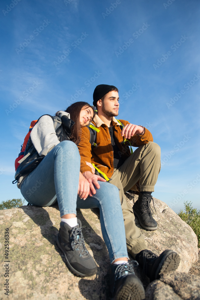 Warm couple hiking in autumn. Man and woman sitting on peak, girlfriend leaning on shoulder. Love, leisure, relationship concept