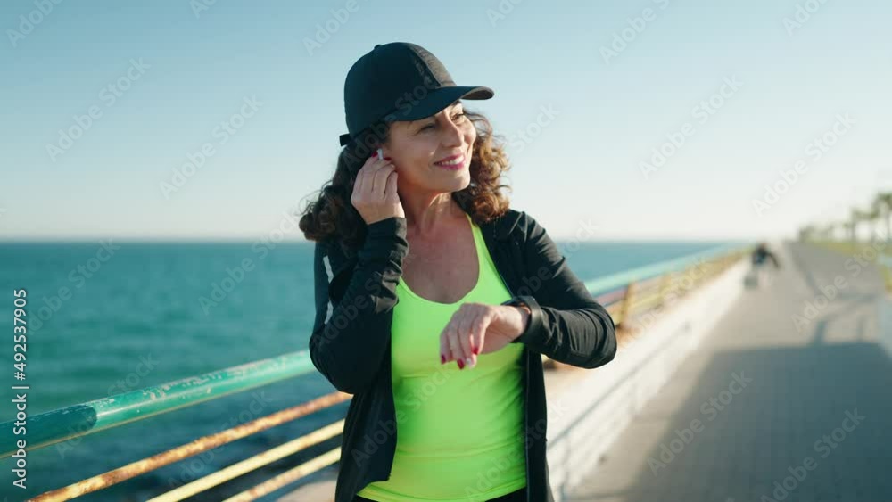 Middle age woman wearing sportswear running and looking stopwatch at seaside Middle age woman wearing sportswear running and looking stopwatch at seaside