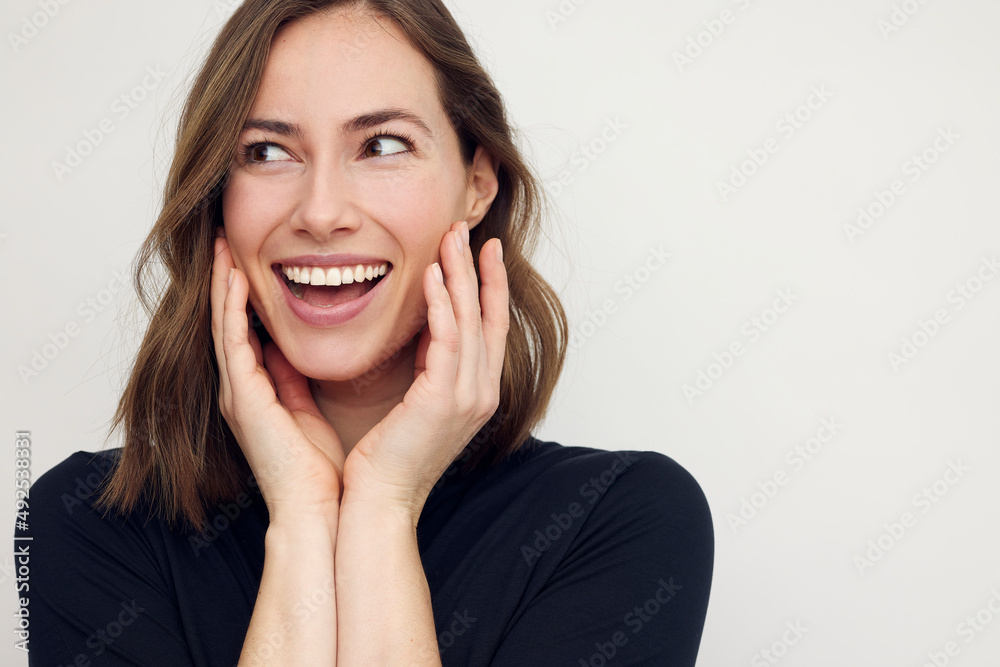 Portrait of a beautiful happy woman smiling and thinking, with hands on her cheeks like she's thinking and making a surprised expression. Female in black with big smile isolated on white background. Portrait of a beautiful happy woman smiling and thinking, with hands on her cheeks like she's thinking and making a surprised expression. Female in black with big smile isolated on white background.