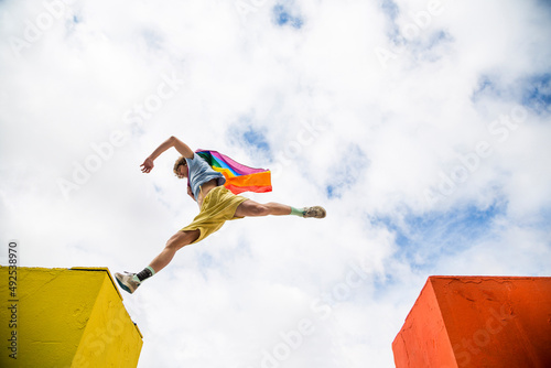 young man jumping through the air with gay pride flag cape on his back photo