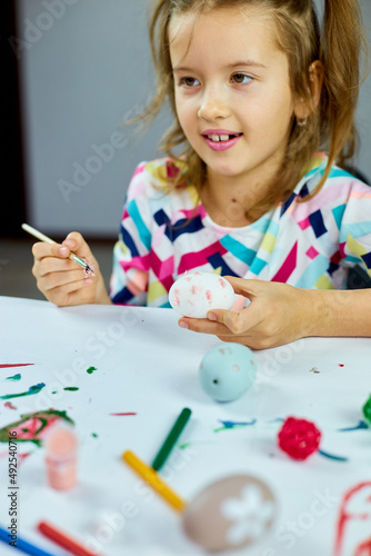 Happy little girl painting, drawing with brush eggs at home.