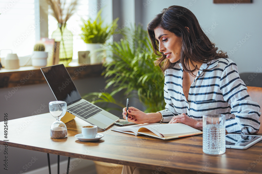 Attractive smiling woman in a shirt sitting relaxed at a table at home and working online on a laptop from home freelancer, social distancing self-isolation communication digital conference