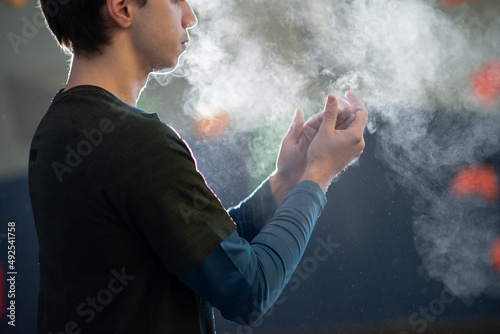 Side view of sportsman powdering hands before climbing. Thoughtful young man in bouldering gym preparing for training standing concentrated on applying powder. Healthy lifestyle and sport concept