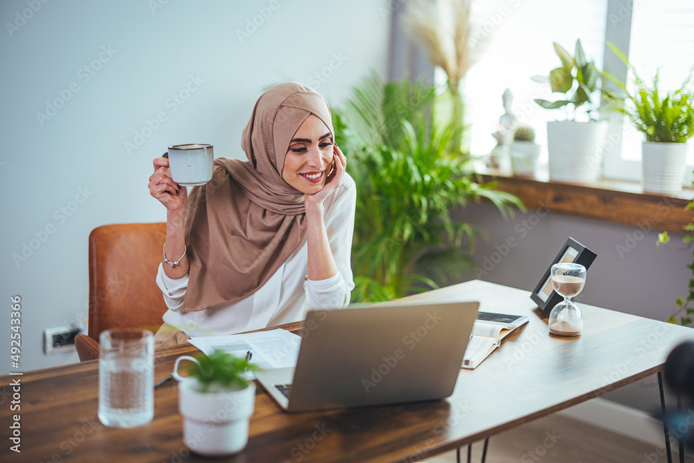 Teleconference. Smiling Muslim woman in hijab has video call on laptop at home, kind Islamic lady in headscarf waves camera, enjoys online communication, copy space Teleconference. Smiling Muslim woman in hijab has video call on laptop at home, kind Islamic lady in headscarf waves camera, enjoys online communication, copy space