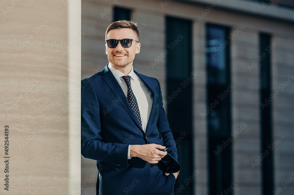 People, business and finances concept. Positive glad satisfied prosperous male director in trendy sunglasses, wears elegant suit, looks happily into distance, being self assured in his success. People, business and finances concept. Positive glad satisfied prosperous male director in trendy sunglasses, wears elegant suit, looks happily into distance, being self assured in his success.