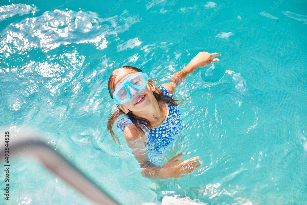 Little girl in goggles having fun, dives and swim in the swimming pool