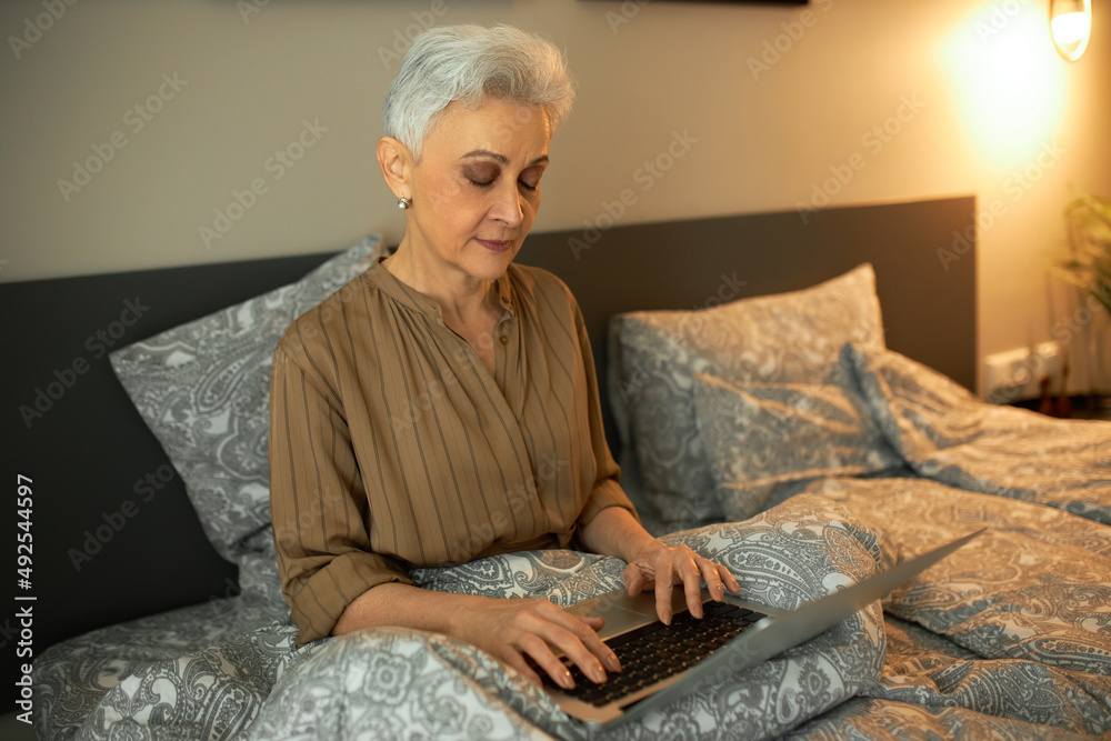Sleepy tired exhausted female writer with grey hair sitting on bed in