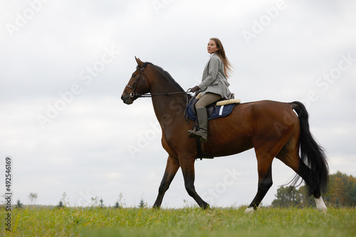 Beautiful young woman riding a horse on the field. Sideways to the camera. Freedom, joy, movement