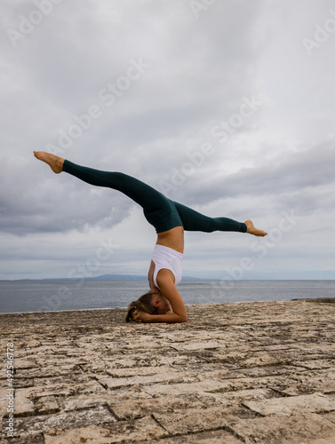 Outdoor yoga practice near the ocean. Young woman practicing Salamba Shirshasana. Yoga Headstand with leg split. Inverted asana. Beautiful asana. Yoga retreat. Copy space. Bali