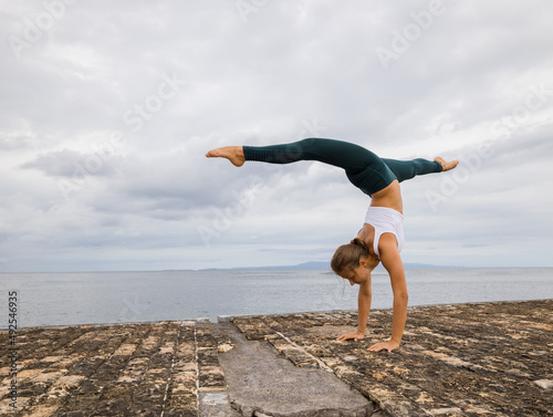 Outdoor yoga practice near the ocean. Young woman practicing Adho Mukha Vrksasana. Yoga Handstand is an inverted asana. Beautiful asana. Flexible slim body. Yoga retreat. Copy space. Bali