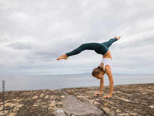 Outdoor yoga practice near the ocean. Young woman practicing Adho Mukha Vrksasana. Yoga Handstand is an inverted asana. Beautiful asana. Strong slim body. Yoga retreat. Copy space. Bali