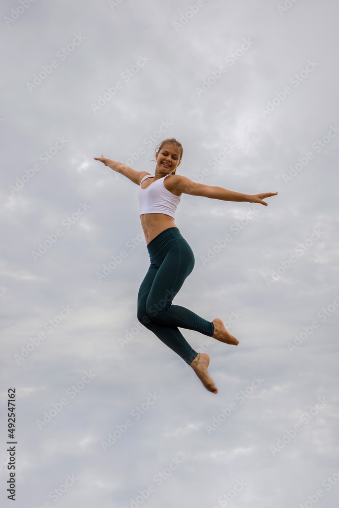 Beautiful young woman jumping over cloudy sky. Caucasian woman wearing sportswear. Fitness, wellness concept. Outdoor activity. Copy space. Sky background. Bali