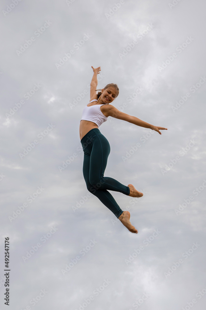Slim Caucasian young woman jumping over cloudy sky. Caucasian woman wearing sportswear. Fitness, sport, wellness concept. Outdoor activity. Copy space. Sky background. Bali
