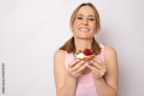 Pensive smiling young woman holding cupcake and standing isolated over white background.