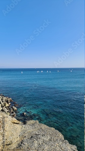 Savona, Italy - February 12, 2022: Panorama of the blue sea, light above the water, ocean sunrise. Some little waves in winter days. Clear sky reflected on the water.