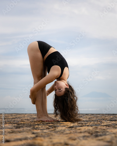 Sportive Caucasian woman doing streatching and warming up on the beach. Standing Forward Bend. Flexible spine. Healthy active lifestyle. Outdoor fitness. Wellness concept. Copy space. Bali