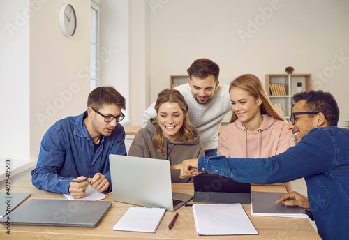 Creative university students sitting at library desk  looking at modern laptop computer  showing  watching  discussing videos  making business  entrepreneurship  marketing group project presentation