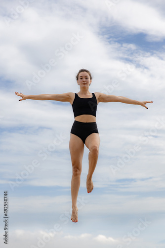 Beautiful young woman jumping over cloudy blue sky. Caucasian woman wearing black sportswear. Fitness, wellness concept. Outdoor activity. Copy space. Sky background. Bali