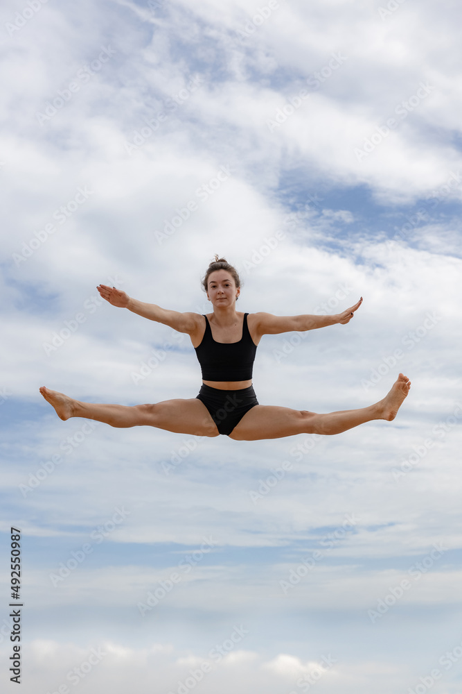 Active energetic cheerful woman jumping over cloudy blue sky. Young Caucasian woman wearing black sportswear. Fitness, wellness concept. Outdoor activity. Copy space. Sky background. Bali Active energetic cheerful woman jumping over cloudy blue sky. Young Caucasian woman wearing black sportswear. Fitness, wellness concept. Outdoor activity. Copy space. Sky background. Bali