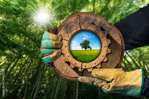 Obraz na płótnie Hands with protective work gloves holding a cross section of a tree trunk with a wooden cogwheel in a green forest