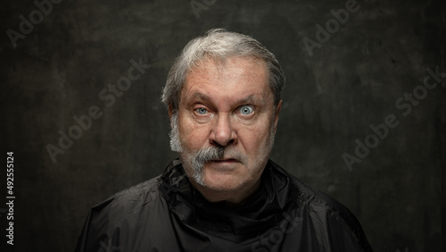 Portrait of surprised senior man looking at camera isolated on dark vintage background. Concept of emotions, fashion, beauty, self-reinvention