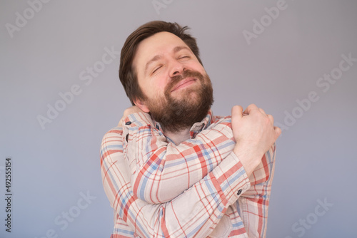 Canvas-taulu Caucasian man with beard hugging oneself happy and positive, smiling confident