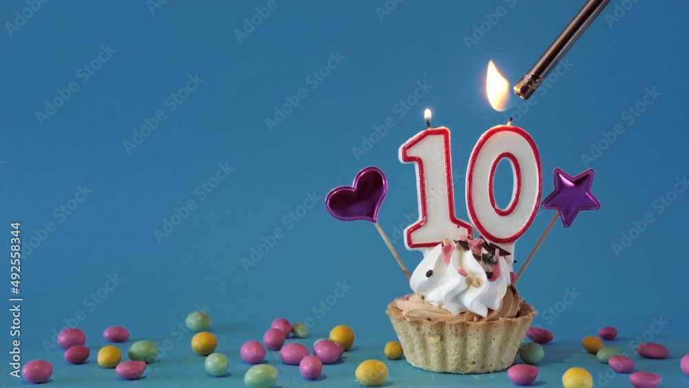 Happy birthday greetings to a 10 year old child, birthday cupcake with candles and birthday decorations on a blue background. Copy space.place for text