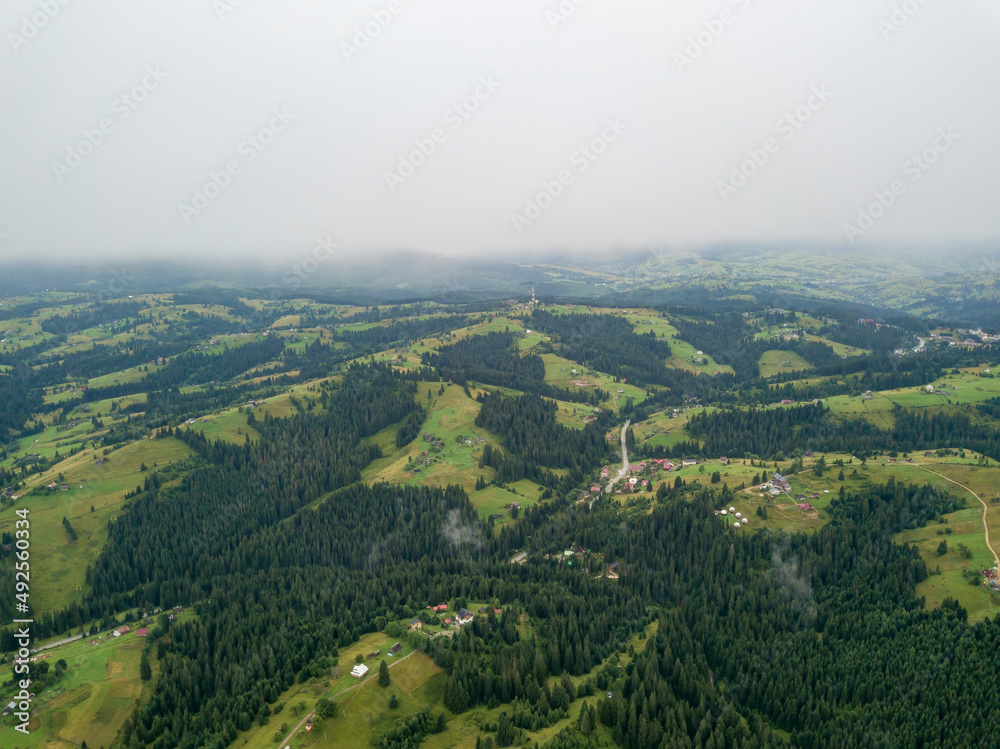 Fototapeta premium Green slopes of Ukrainian Carpathian mountains in summer. Cloudy morning, low clouds. Aerial drone view.