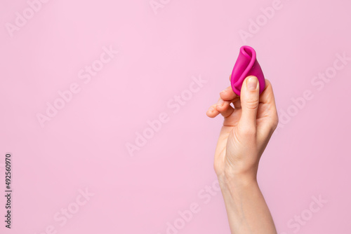 Mature content A young woman folding a pink menstrual cup in her hand. Pink colored background. Space for text. Eco-friendly silicone women's health cycle photo