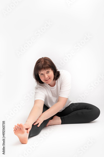 Plus size young brunette woman doing stretching exercise and looks at the camera. Portrait of girl on white background engaged in gymnastics.