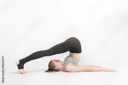 Halasana. Plow Pose. Young woman during a yoga class. Side view. Yoga trainer shows technique of performing asana on white background. photo