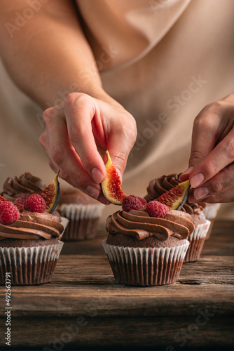 Pastry chef decorates muffin with raspberries and figs. Close up photo of cupcakes preparation. Vertical frame