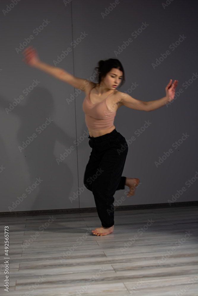 Photo of dancing long-haired blonde girl in torn jeans on brown background