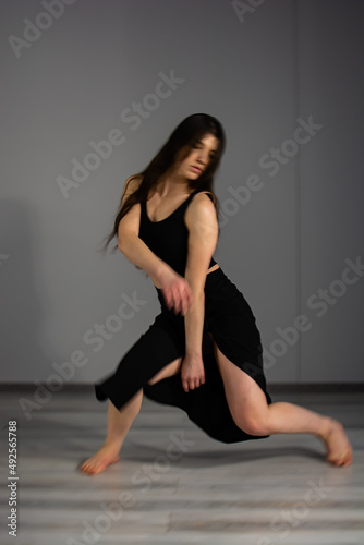 Photo of dancing long-haired blonde girl in torn jeans on brown background