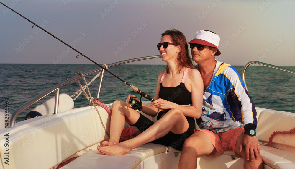 A man 45-46 years old and a woman 30-35 years old on an evening fishing trip in the sea on a high-speed boat. A man embraces a woman. The woman smiles.