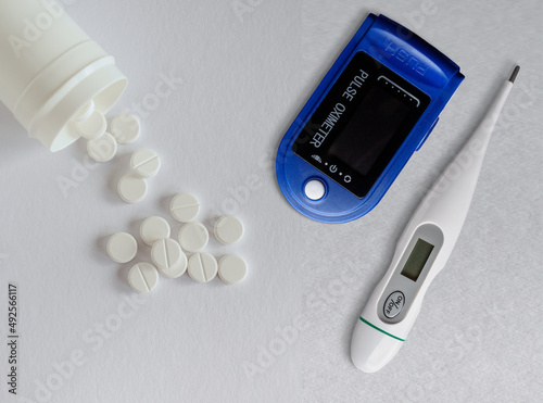 Digital pulse oximeter , thermometer and white pills on white background. Overhead view with copy space