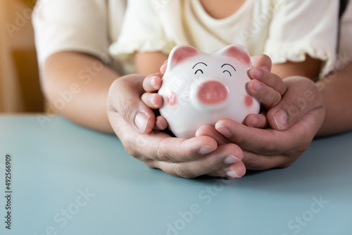 Adult and kid hands holding a piggy bank in savings concept