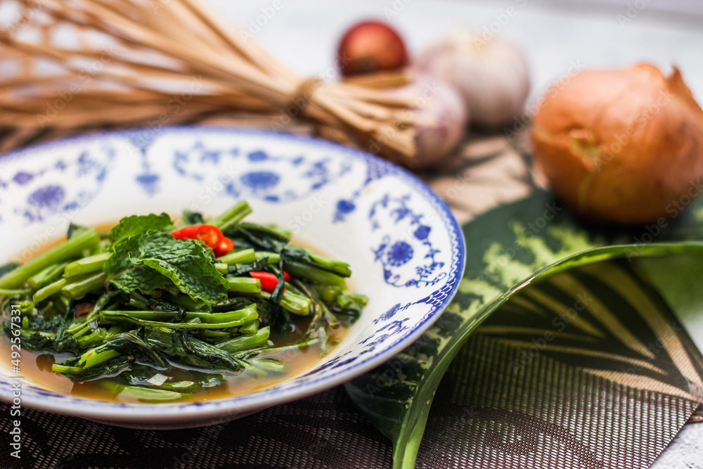 Stir Fried Morning Glory with Soybean Paste Served in a Chinese-patterned dish with spotted leaves, onions, shallots on the table. Stir Fried Morning Glory with Soybean Paste Served in a Chinese-patterned dish with spotted leaves, onions, shallots on the table.