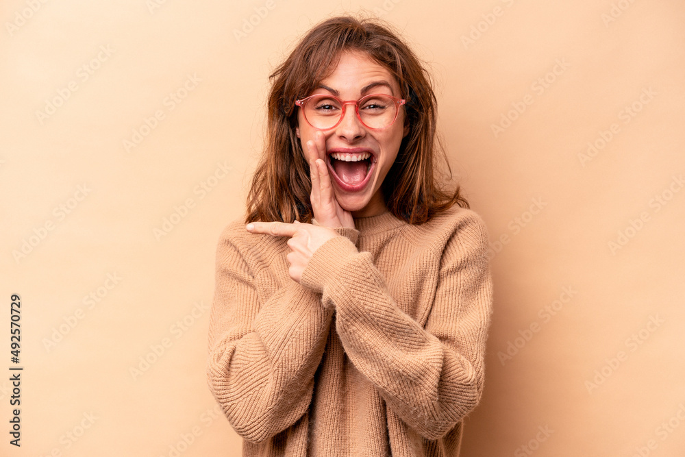 Young caucasian woman isolated on beige background saying a gossip, pointing to side reporting something. Young caucasian woman isolated on beige background saying a gossip, pointing to side reporting something.