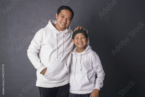 Father and son smiling and standing together wearing white hoodie for apparel mock up, isolated on gray background 