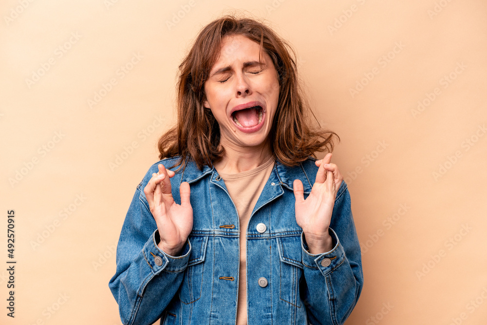 Young caucasian woman isolated on beige background crossing fingers for having luck Young caucasian woman isolated on beige background crossing fingers for having luck