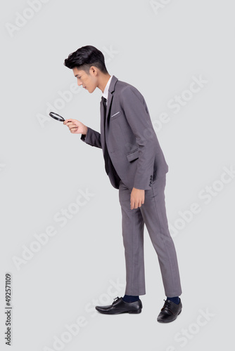 Young asian business man in suit look at magnifying glass for search isolated on white background, businessman expression and find quality, full length, inspector and scrutiny, male expression.