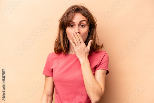 Young caucasian woman isolated on beige background shocked, covering mouth with hands, anxious to discover something new.
